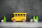 Yellow wooden school bus eco-friendly toy with smiling passengers, trees, and stones
